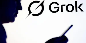 Getty Images Silhouette of a person holding a smartphone in front of Grok and X logo