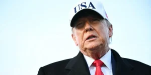 s US President Donald Trump speaks to journalists upon returning to Joint Base Andrews in Maryland. He is wearing a white hat with the words USA on it