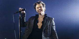 m colorida de Harry Styles em show, sorrindo e usando roupa toda preta