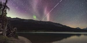 a white streak of light through a starry sky. there is also some faint green auroras and STEVE