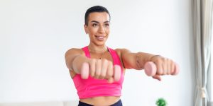 Domestic Training With Weights. Positive black lady doing exercises with dumbbells, strengthening her body at home. Smiling young female working on her biceps muscles, staying healthy