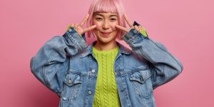 always-stay-bright-positive-optimistic-woman-shows-peace-sign-eyes-sends-positive-vibes-you-wears-green-sweater-denim-jacket-expresses-happiness-joy-summer-holidays-feels-rejoice