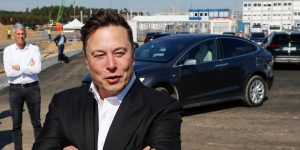 Elon Musk crosses his arms over his chest as he stands in front of a Tesla