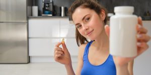 feche-o-retrato-de-uma-jovem-instrutora-de-fitness-mostrando-uma-garrafa-de-vitaminas-tomando-brotos