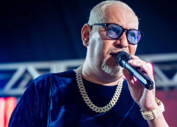 Chrigor Lisboa no palco, cantando. Ele veste uma blusa azul e uma corrente no pescoço, além de óculos azul (Reprodução Instagram Chrigor Lisboa