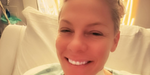 Pink sorrindo, com curativo no pescoço em uma cama de hospital (Reprodução Instagram Pink