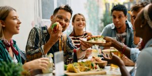 (Créditos: razen Zigic / iStock)  Young happy people having lunch together. Focus is on man passing tacos to his female friend.