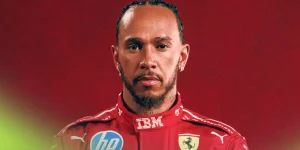 A portrait of Lewis Hamilton wearing Ferrari overalls against a red background