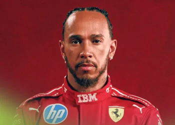 A portrait of Lewis Hamilton wearing Ferrari overalls against a red background