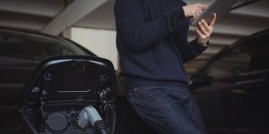 Man using digital tablet while charging electric car in garage