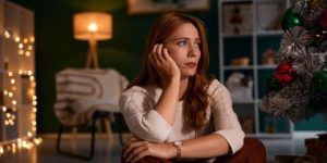 Jovem sentada no chão ao lado de uma árvore de Natal em casa  • Getty Images