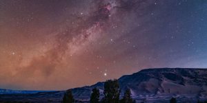 The glowing band of the Milky Way's galactic plane is pictured tumbling diagonally through a starry night sky above a mountainous region
