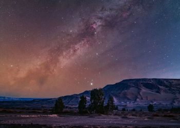 The glowing band of the Milky Way's galactic plane is pictured tumbling diagonally through a starry night sky above a mountainous region
