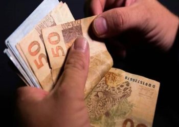 colorida de duas mãos segurando um maço de dinheiro PIS Pasep